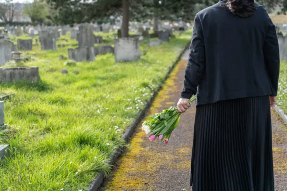 Female mourner dressed in black carrying flowers at a funeral graveyard