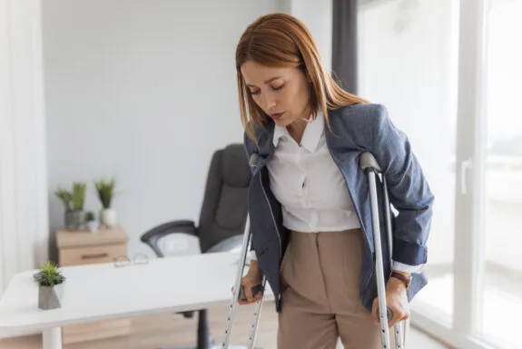 Businesswoman is walking on crutches in the office after suffering a leg injury